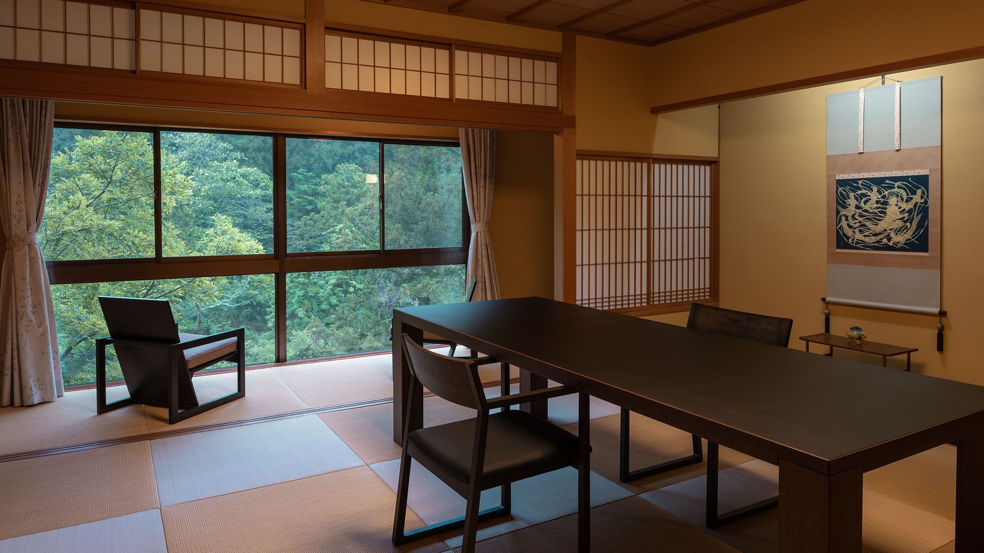 A traditional Japanese room with tatami flooring, a low table, and a view of trees through large windows.