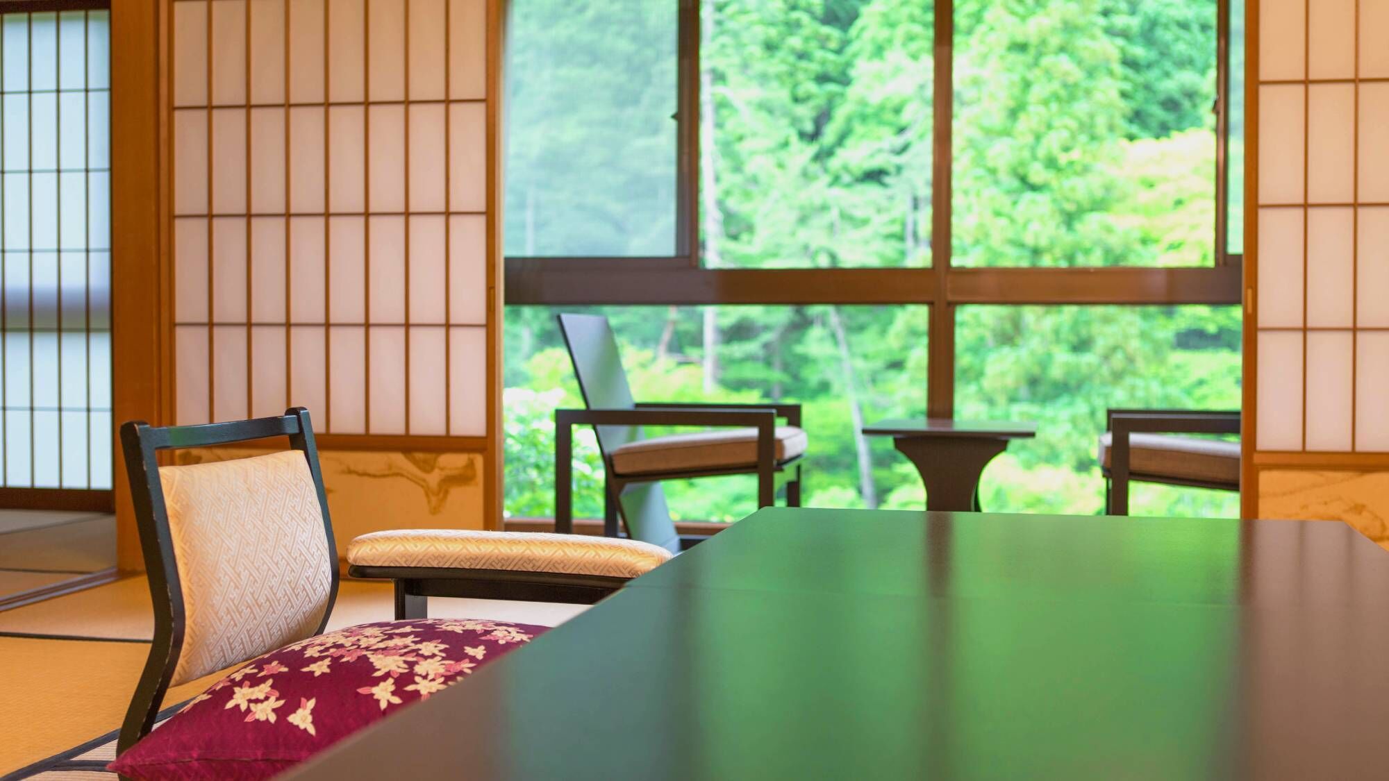 A traditional Japanese room with tatami flooring, a low table, and a view of greenery through large windows.