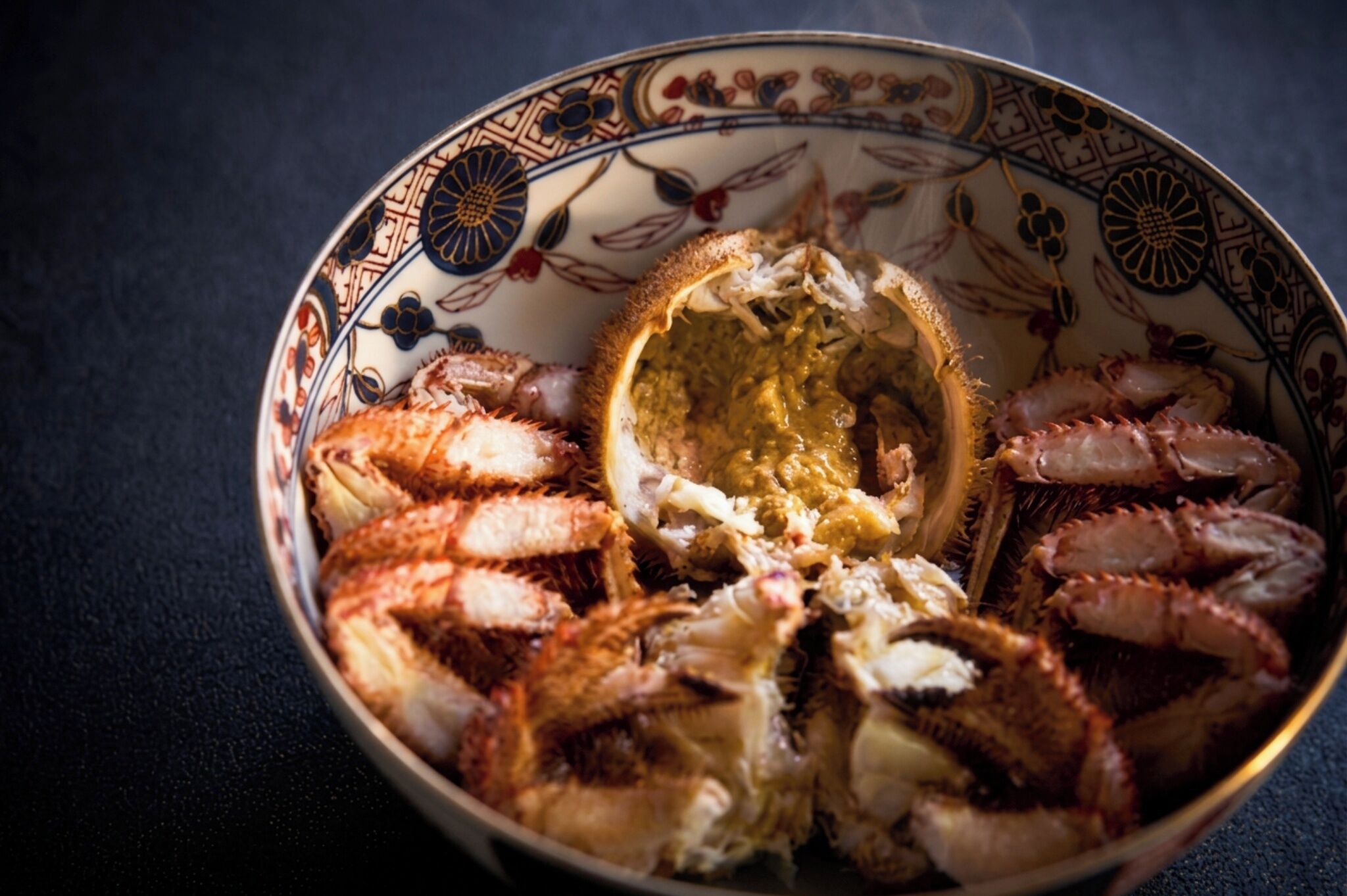 Eine Schüssel mit gekochtem Krabbenfleisch, verziert mit einem Muster, auf einer dunklen Unterlage.