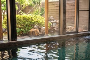 A pool with clear water, surrounded by a wooden deck and a view of a garden with rocks and greenery. - Kocho (Kaga)