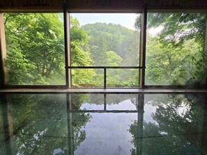 A room with a large window offering a view of a forested area. - Kocho (Kaga)