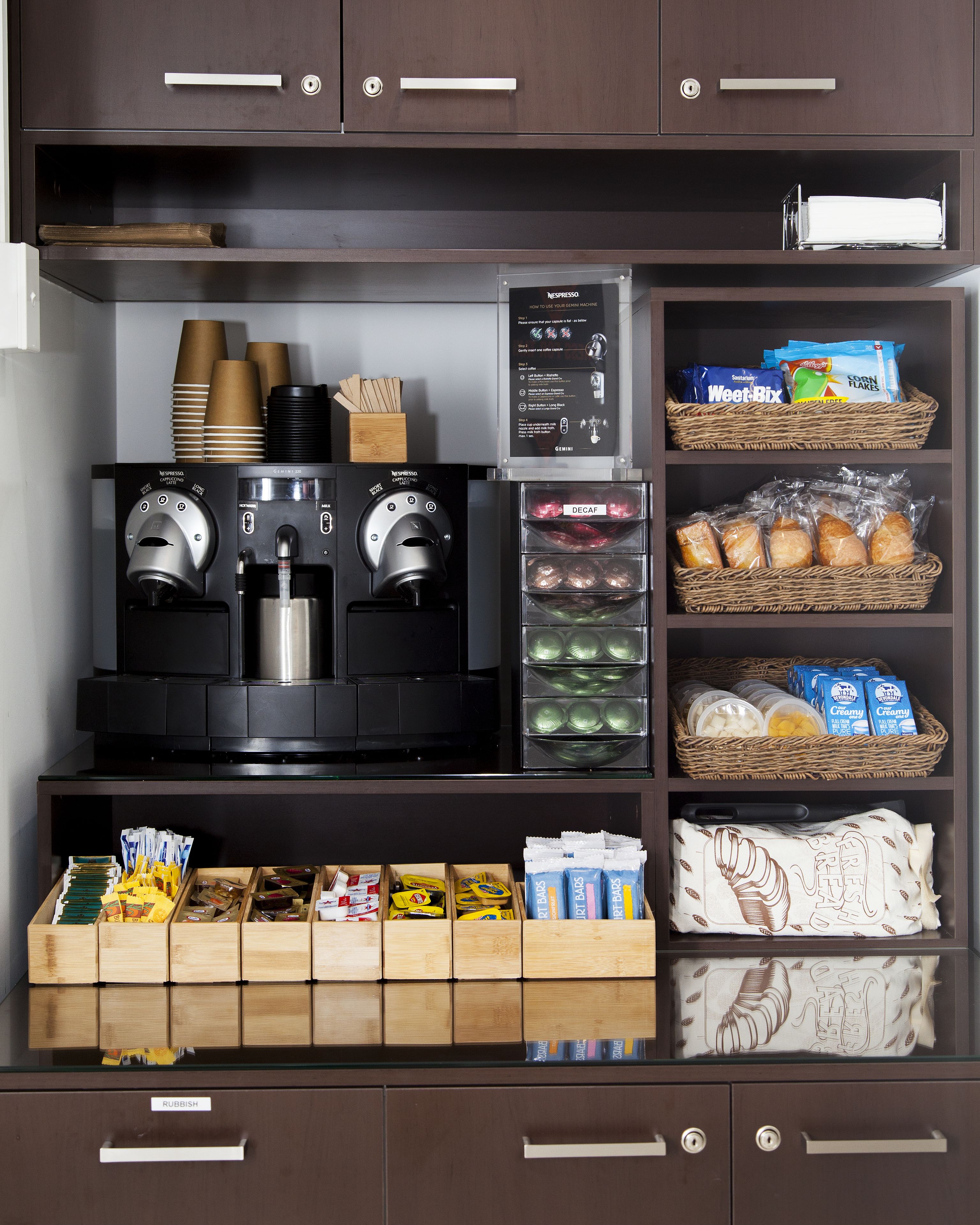 A coffee station with two espresso machines, a coffee grinder, and a variety of coffee pods and creamer options.