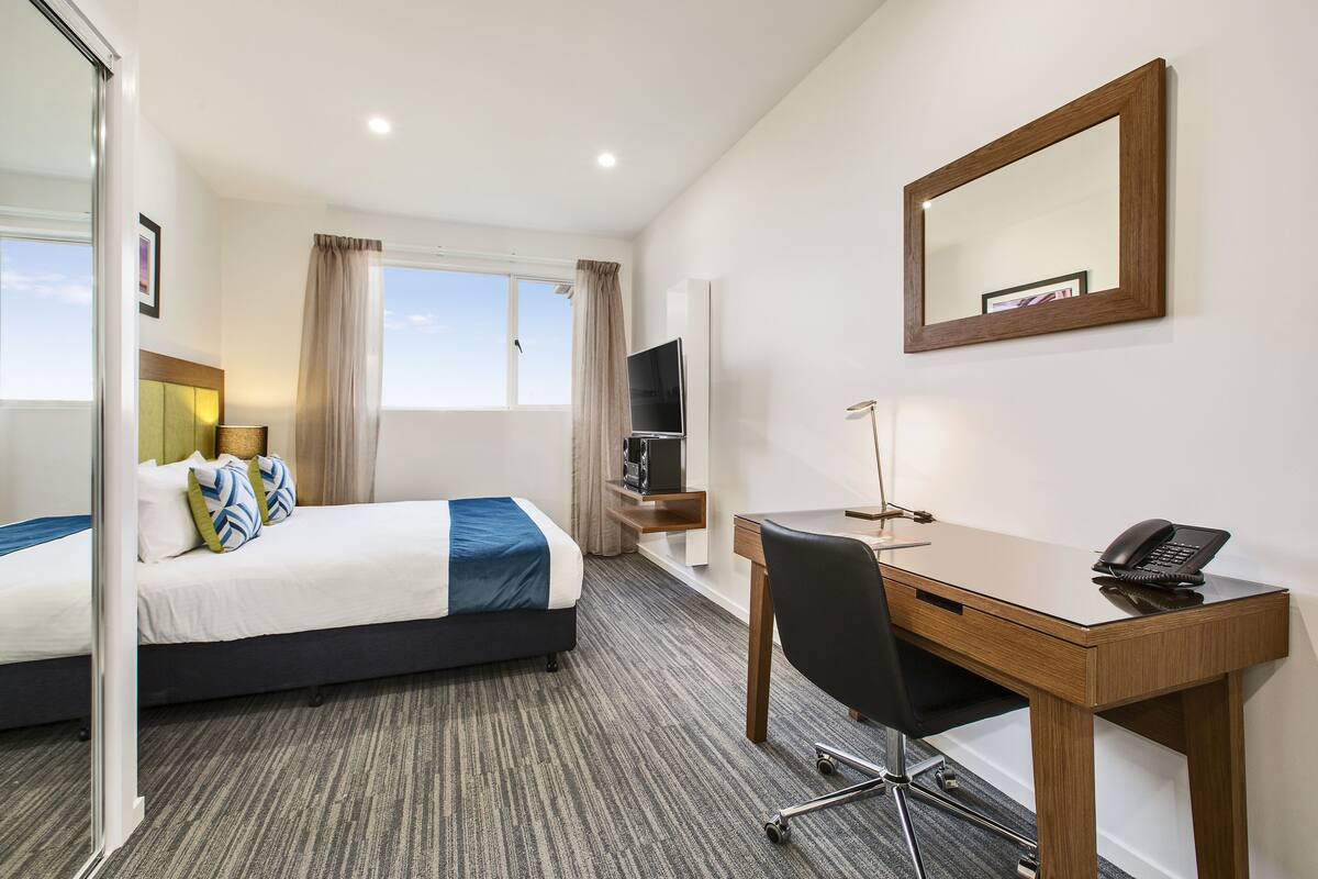 A hotel room with two beds, a desk, a chair, a TV, and a mirror.