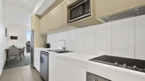 A modern kitchen with white cabinetry, a built-in microwave, a sink, and a dishwasher. - Quest Chermside on Playfield (Chermside)