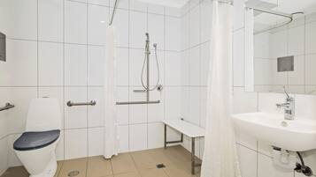 Een badkamer met toilet, douche, bankje en wastafel.