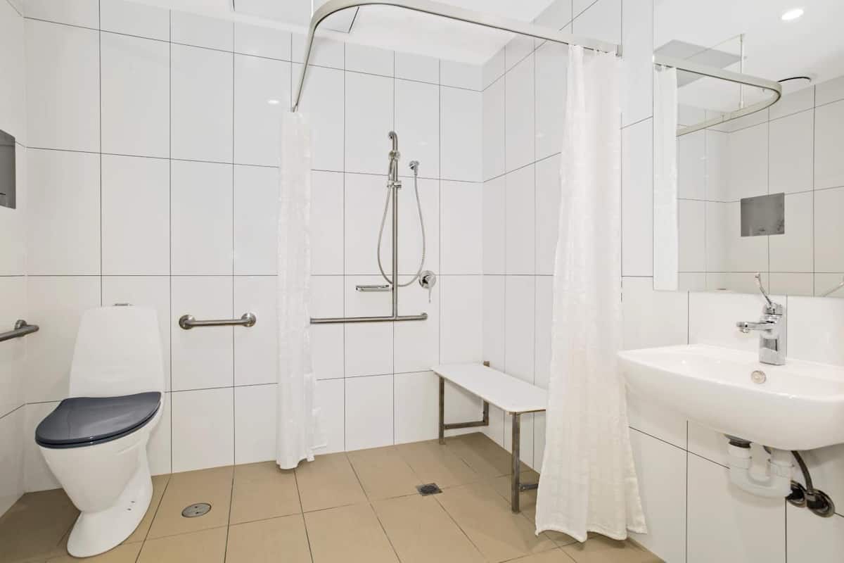 A modern bathroom with a toilet, shower, bench, and sink.