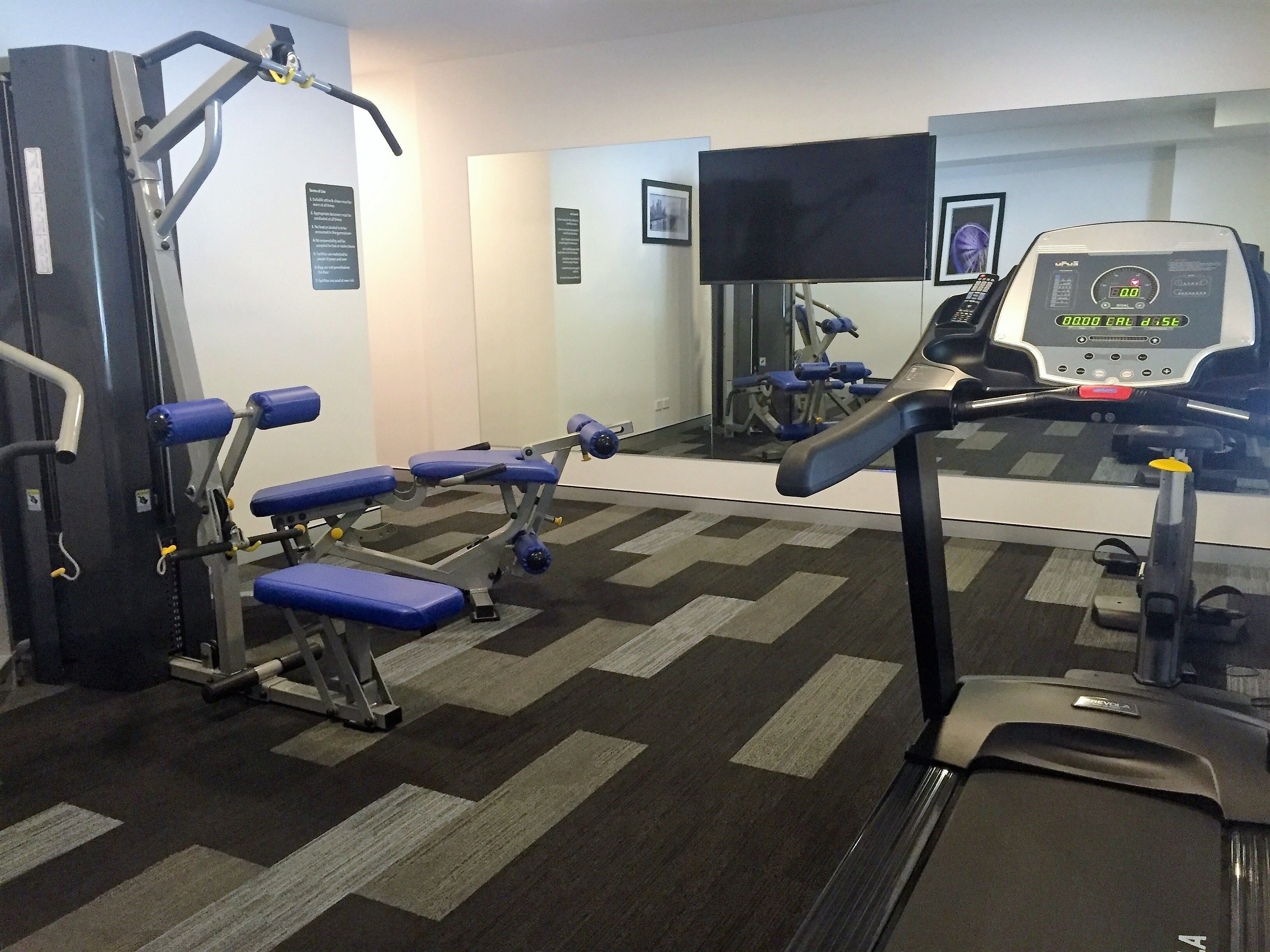 A gym with exercise equipment, a treadmill, and a digital display.