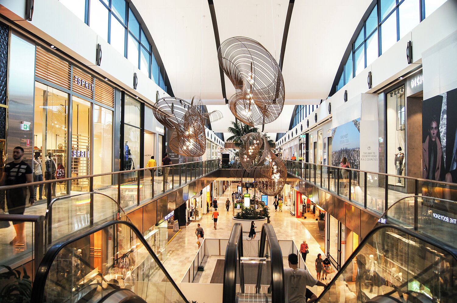 A multi-level shopping mall with glass railings, escalators, and modern interior design.