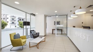 A modern hotel lobby with a reception desk, seating area, and large windows offering views of the city. - Quest Chermside on Playfield (Chermside)