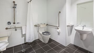A modern bathroom with a shower, toilet, and sink, featuring grab bars and a white tiled floor.
