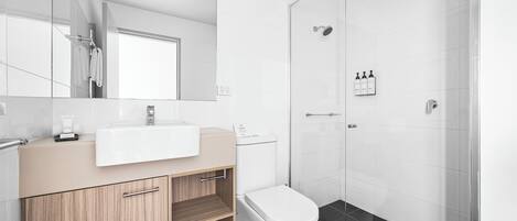 A modern bathroom with a glass shower enclosure, a white sink, and a wooden vanity.