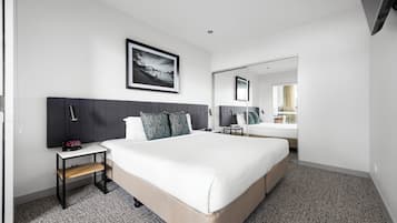 A modern hotel room with a large bed, a bedside table with a lamp, a framed picture on the wall, and a mirror reflecting part of the room.