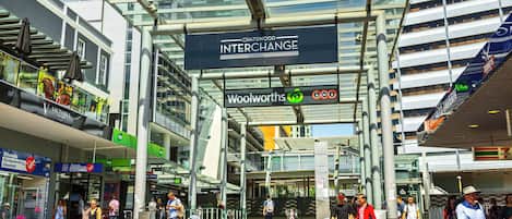 Una plaza urbana moderna con un letrero destacado que dice 'Chatswood Interchange', rodeada de edificios altos y diversas tiendas.