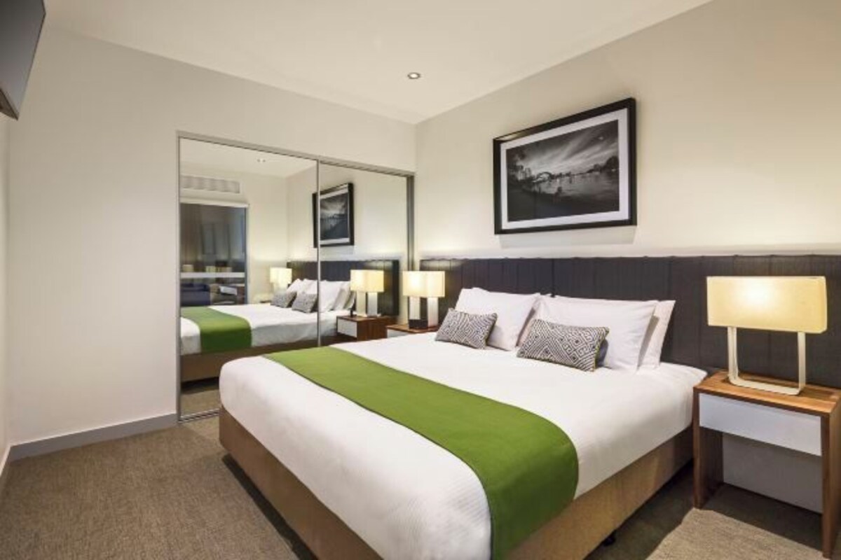 A hotel room with a large bed, a mirror, a framed picture on the wall, and two bedside tables with lamps.