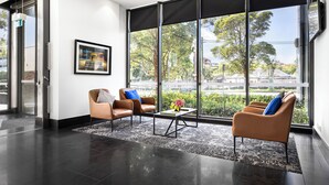 Un vestíbulo moderno con dos sillones de cuero, una mesa de centro y un ventanal con vistas a árboles y edificios.