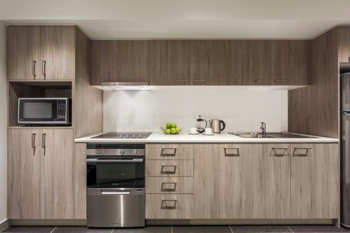 A modern kitchen with wooden cabinets, stainless steel appliances, and a white countertop.