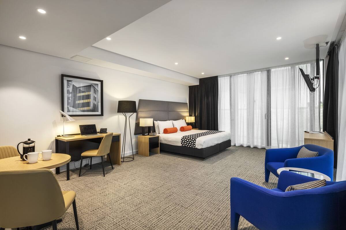 A hotel room with a bed, desk, chairs, and a large window with curtains.
