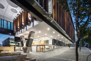 A modern hotel with a prominent 'QUEST' sign, large windows, and a well-lit entrance area.