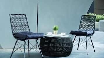 Two black wicker chairs with blue cushions and a round black table with a small plant.