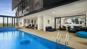 A modern indoor pool area with a view of the city, furnished with sofas and a coffee table. - Quest St Leonards (St. Leonards)