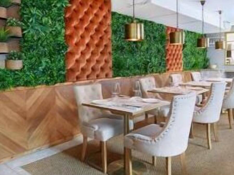 A modern restaurant with a green wall, wooden paneling, and white upholstered chairs.