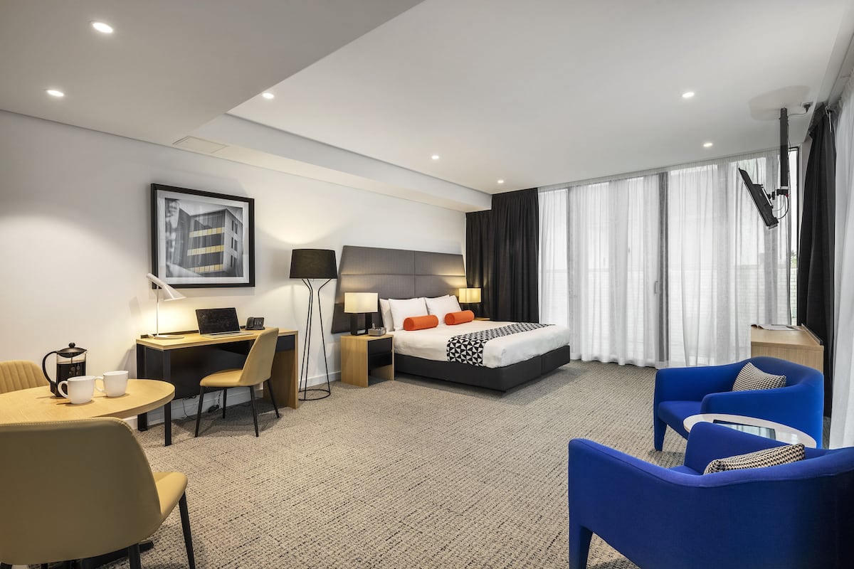 A hotel room with a bed, desk, chairs, and a large window with curtains.