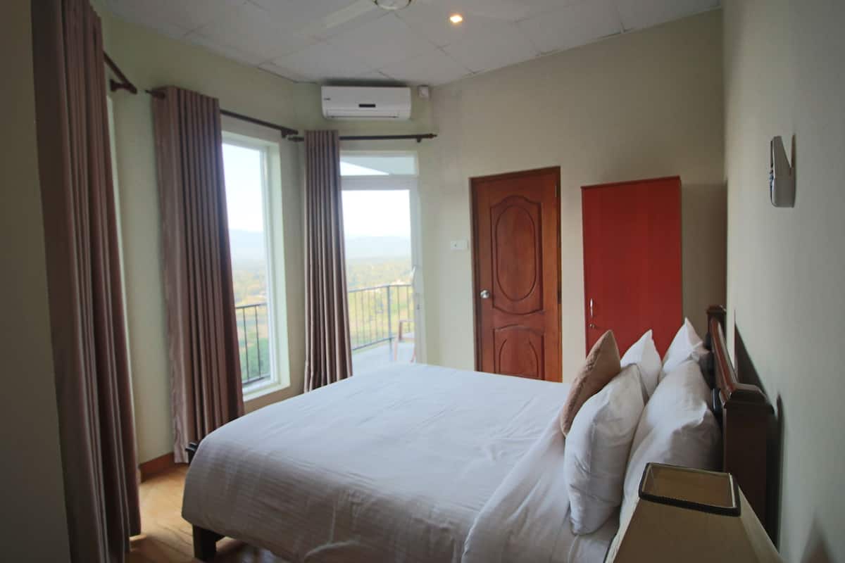 A hotel room with a large bed, a wooden headboard, a red door, and a window with curtains.