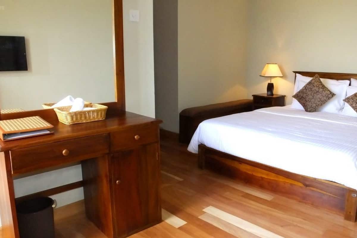 A hotel room with a wooden desk, a bed with white linens, and a nightstand with a lamp.