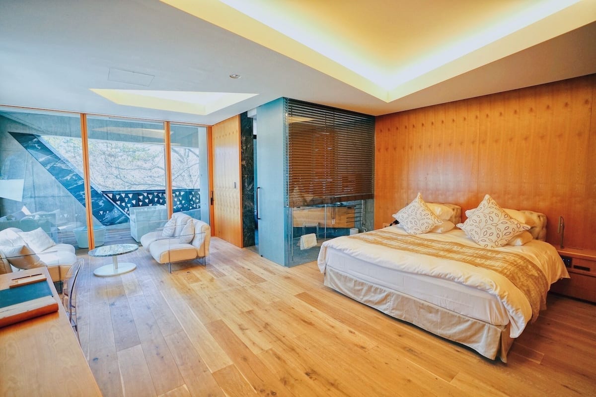Un dormitorio moderno con una cama grande, un sofá y un ventanal de vidrio que da a un balcón.