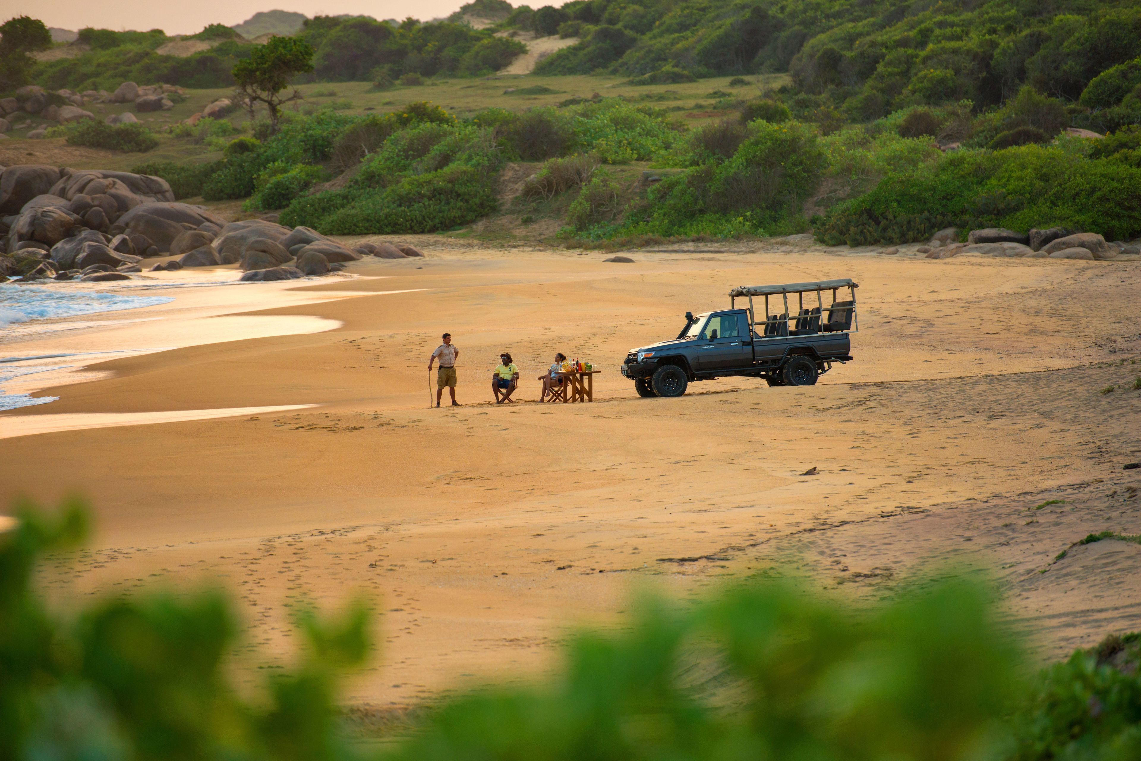Un véhicule de safari est garé sur une plage de sable, et quelques personnes se trouvent à proximité.