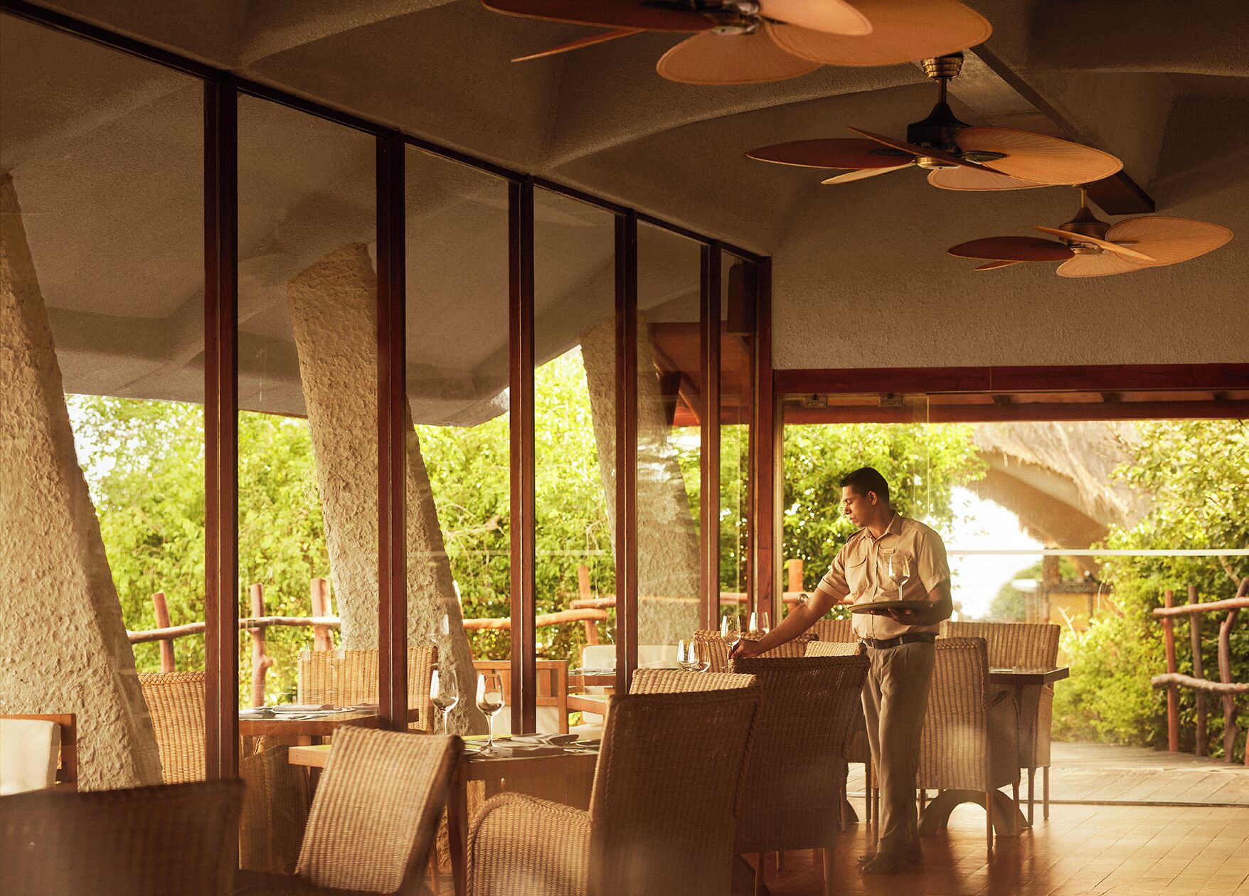 Un restaurante con amplios ventanales, mobiliario de mimbre y ventiladores de techo.