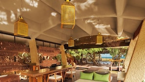 Amplia zona de estar con mobiliario de madera, un bar y vistas a la playa.
