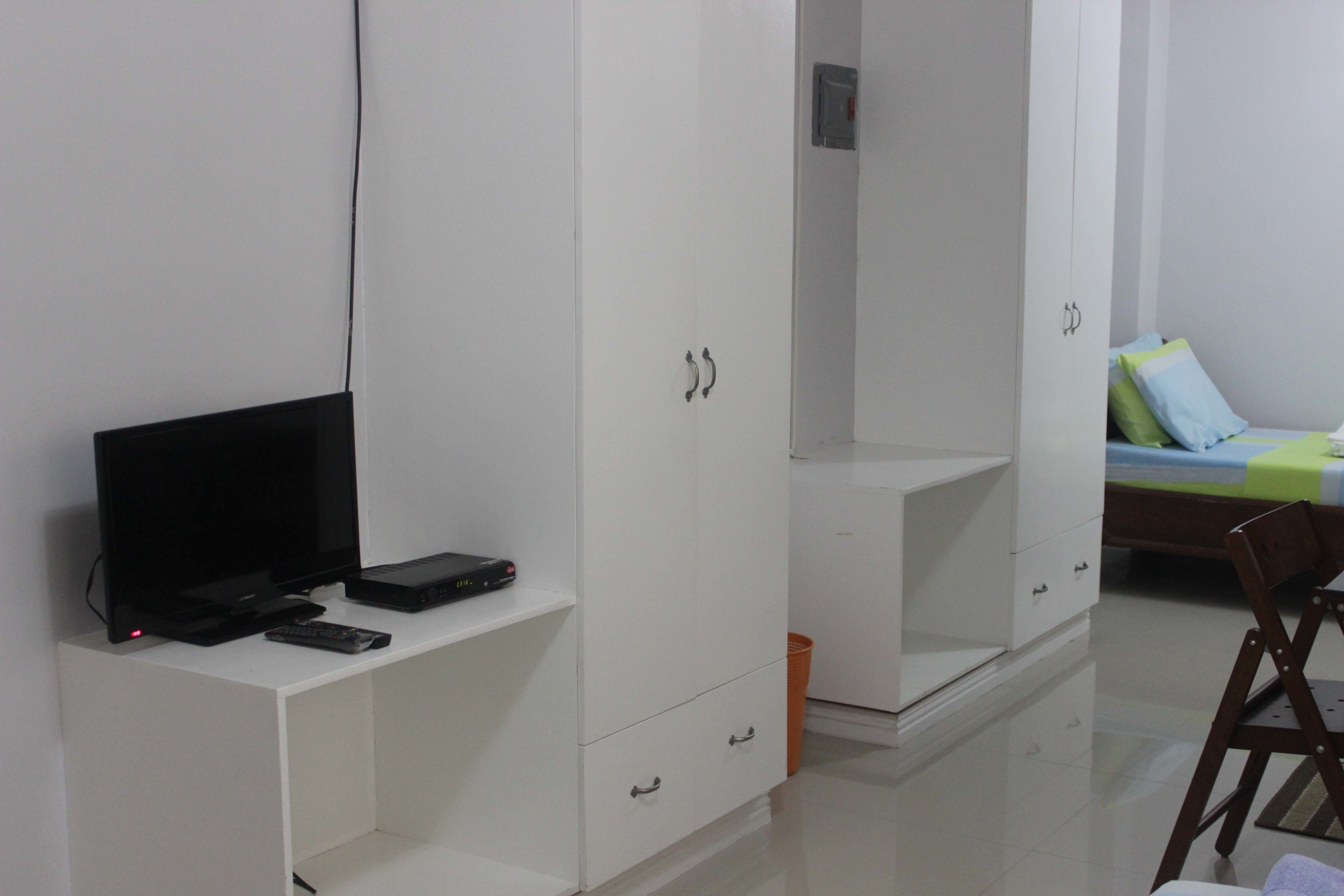 A bedroom with a bed, a TV, a desk, and a wardrobe.