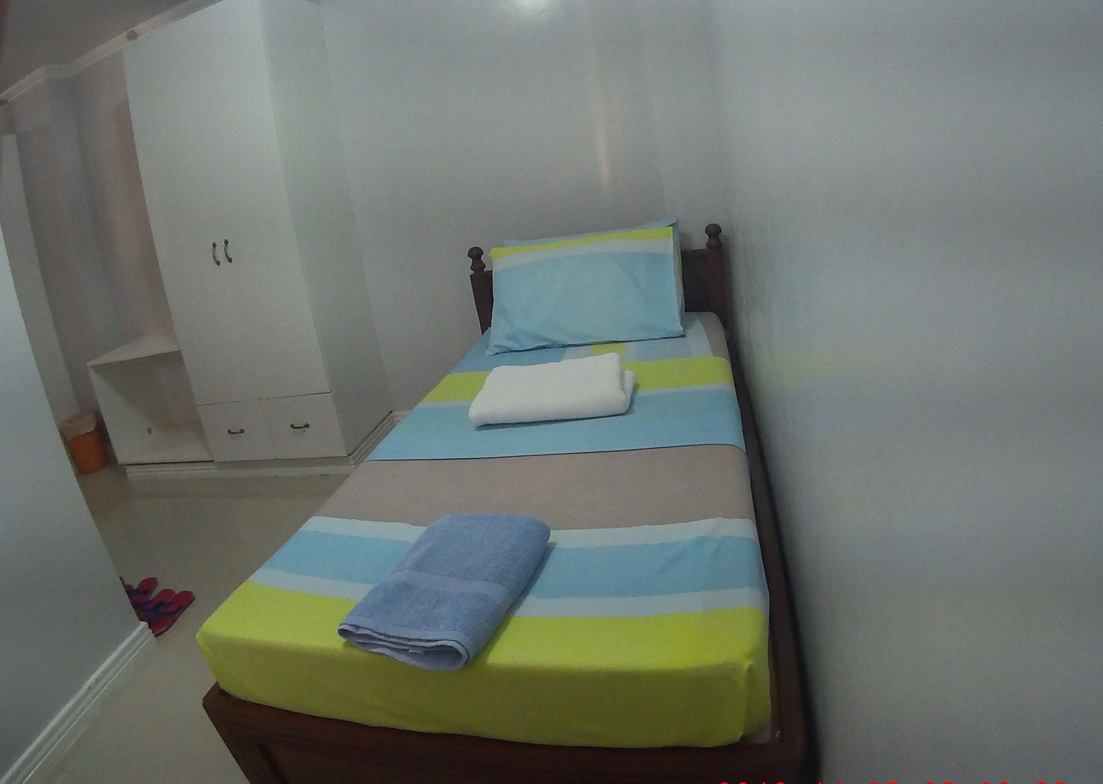 A small, neatly made bed with striped bedding and a folded towel on the footboard.