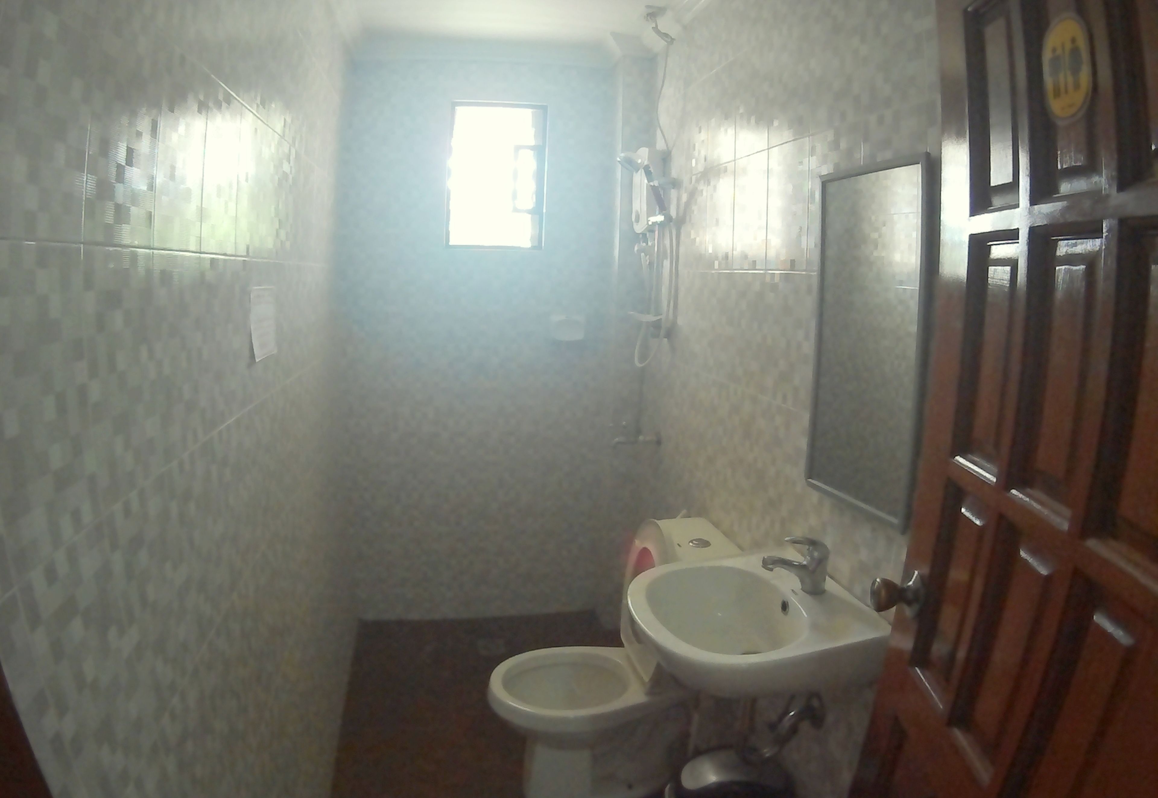 Un baño pequeño con inodoro, lavamanos y ducha. Una ventana proporciona luz natural.