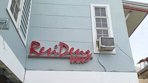 De gevel van herverblijfplaats ReniDeng, met een opvallend bord, airconditioners en een overdekte ingang met potplanten.