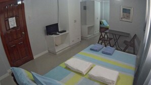 Een slaapkamer met een bed, een bureau met een computer, een kledingkast en een stoel.