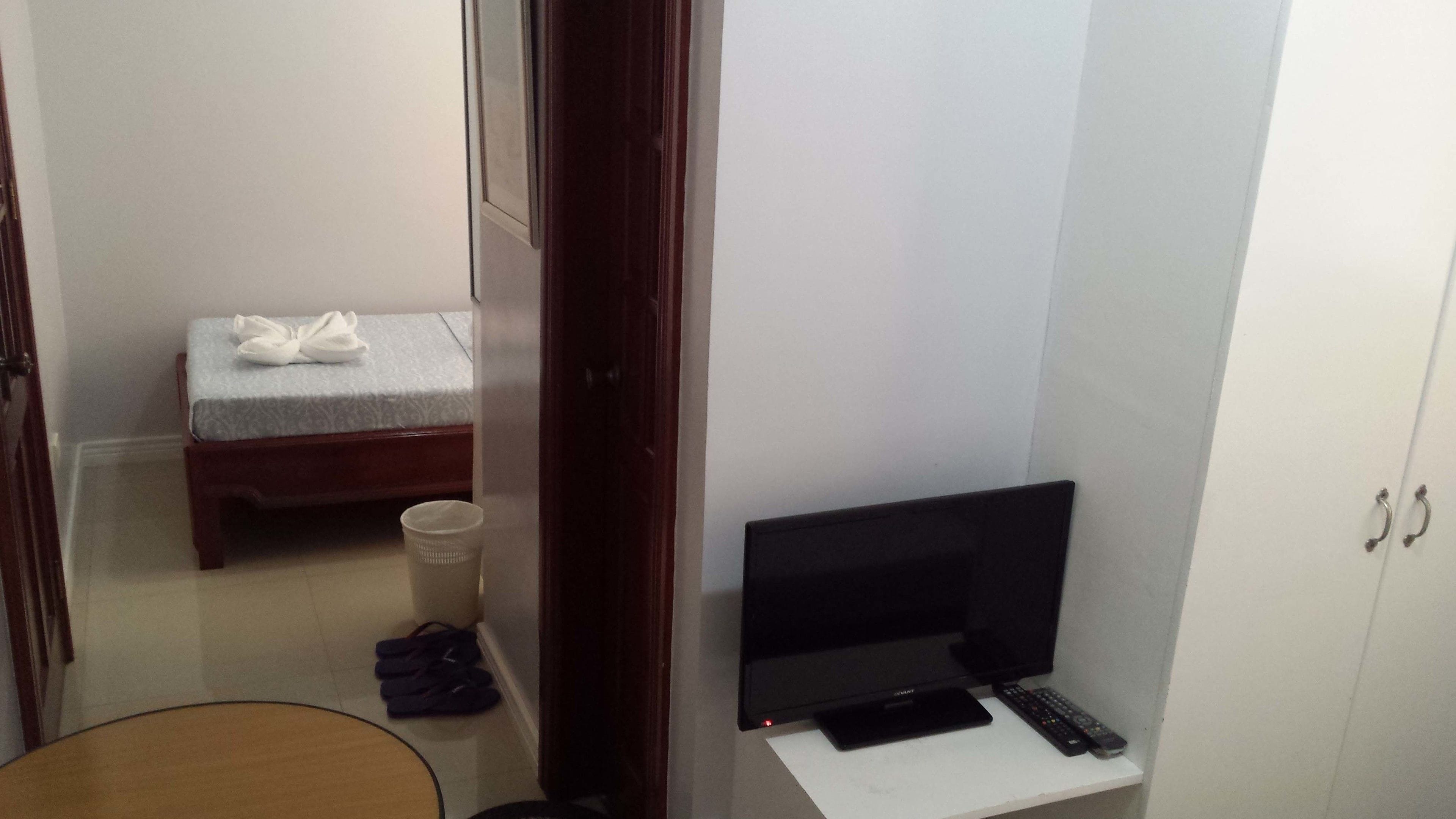 Una habitación pequeña con una cama, un televisor y un escritorio con un control remoto.