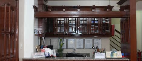 A reception area with a wooden counter, framed certificates on the wall, and a sign indicating the reception desk.