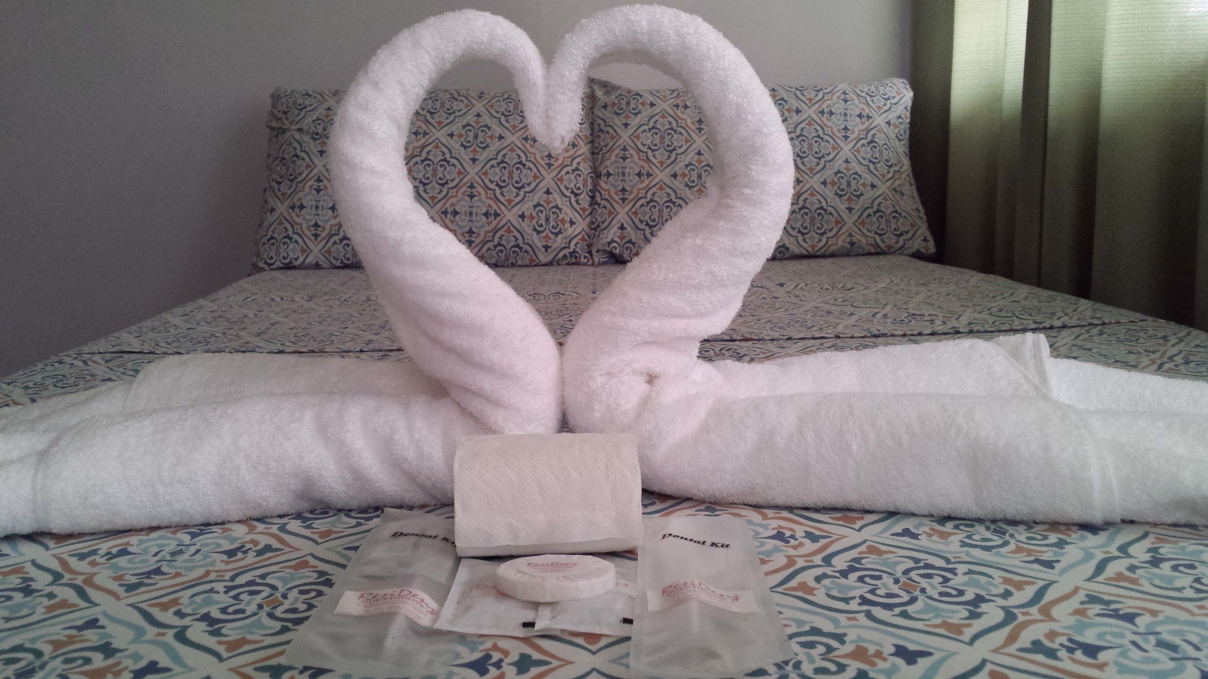 A bed with a decorative towel arrangement in the shape of a heart, a small wooden block, and a tissue box.