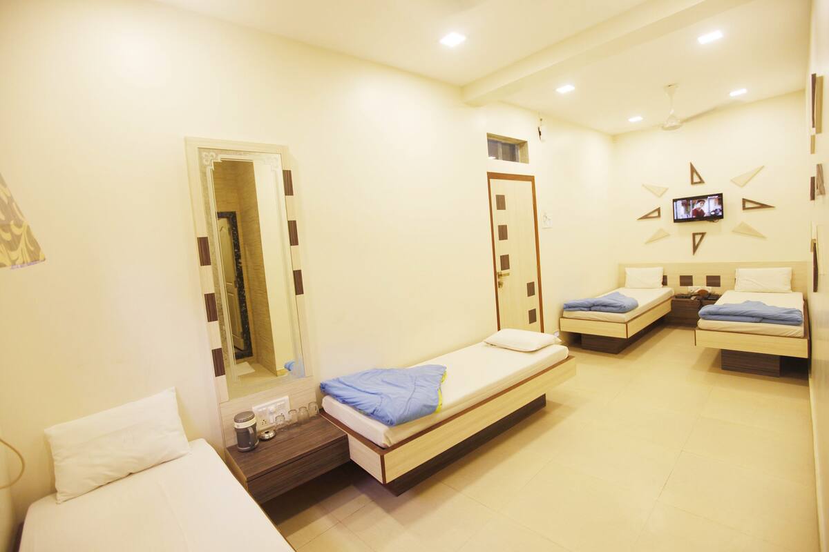 A hotel room with two single beds, a small table with a coffee maker, a mirror, and a TV mounted on the wall.