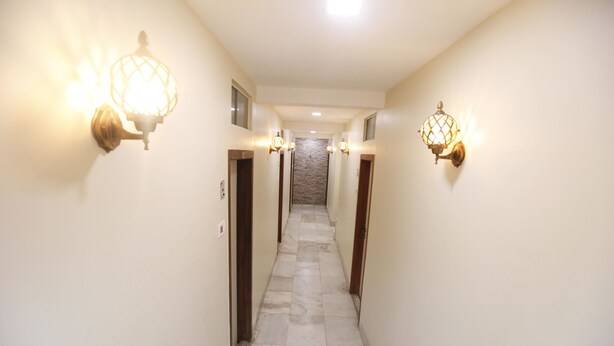 A hallway with light fixtures on the walls, a tiled floor, and a door at the end. - Hotel Al Moazin (Mumbai)