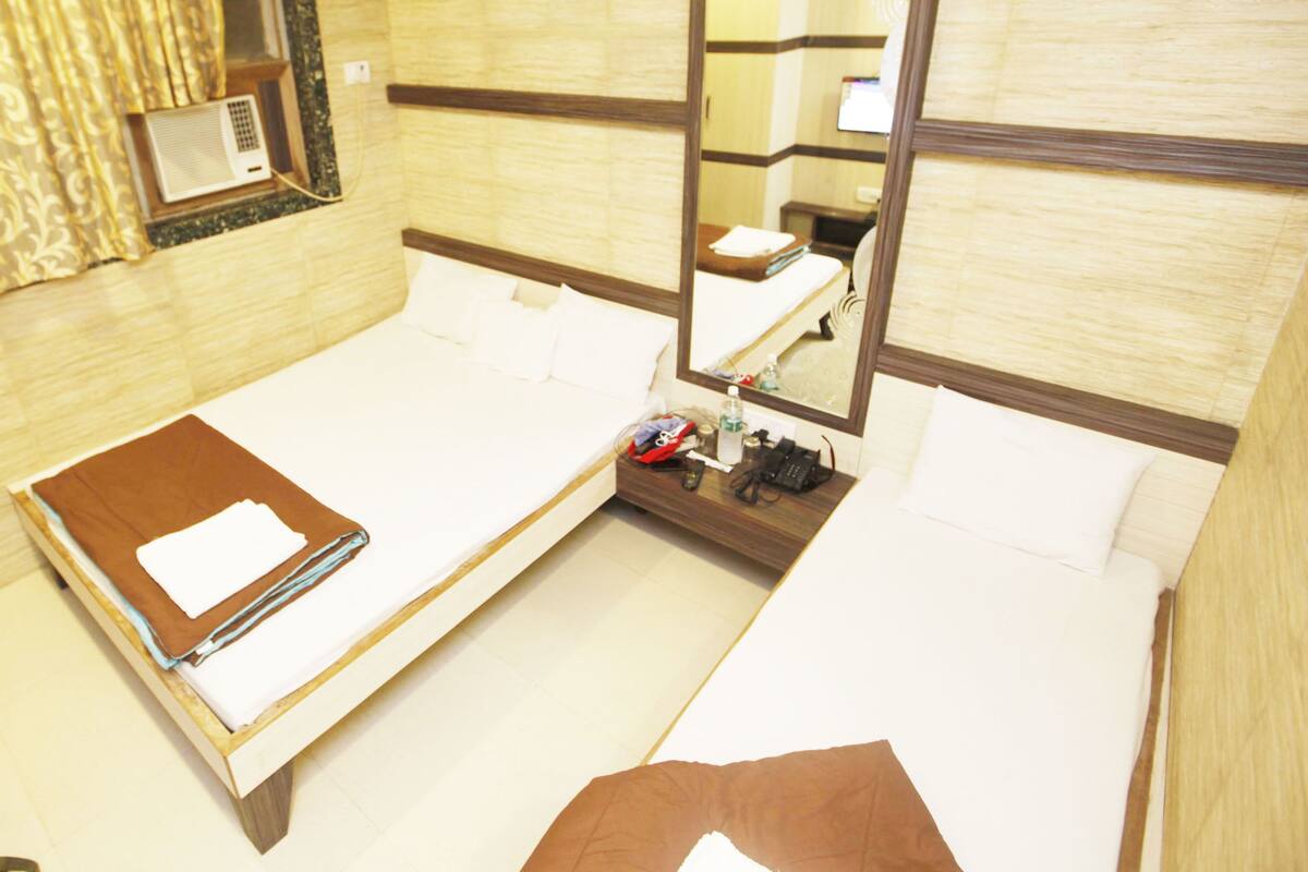 A hotel room with two beds, a bedside table, a mirror, and a window with curtains.