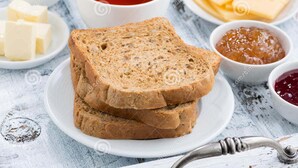 A plate with slices of whole grain bread, butter, jam, and cheese on a rustic table. - Hotel Al Moazin (Mumbai)