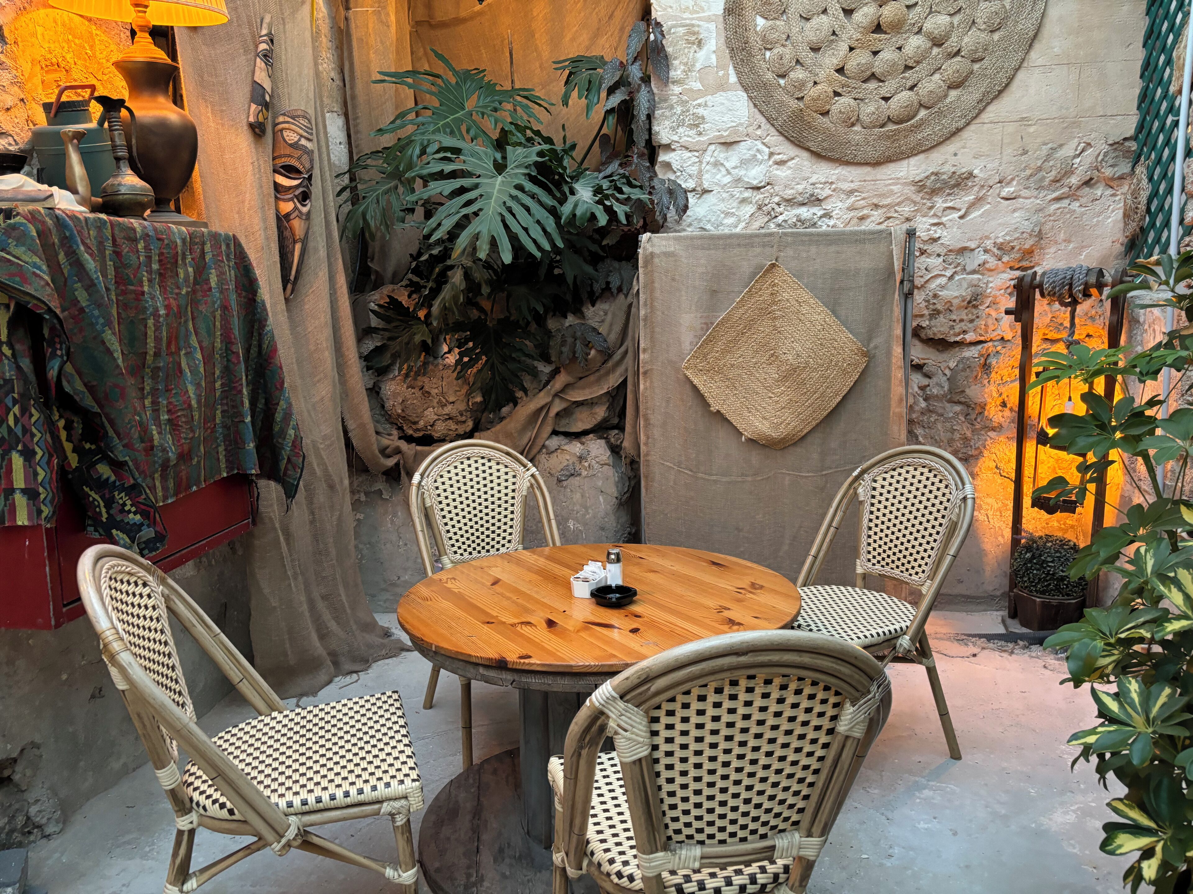 A cozy outdoor seating area with wicker chairs and a wooden table, surrounded by decorative elements and plants.