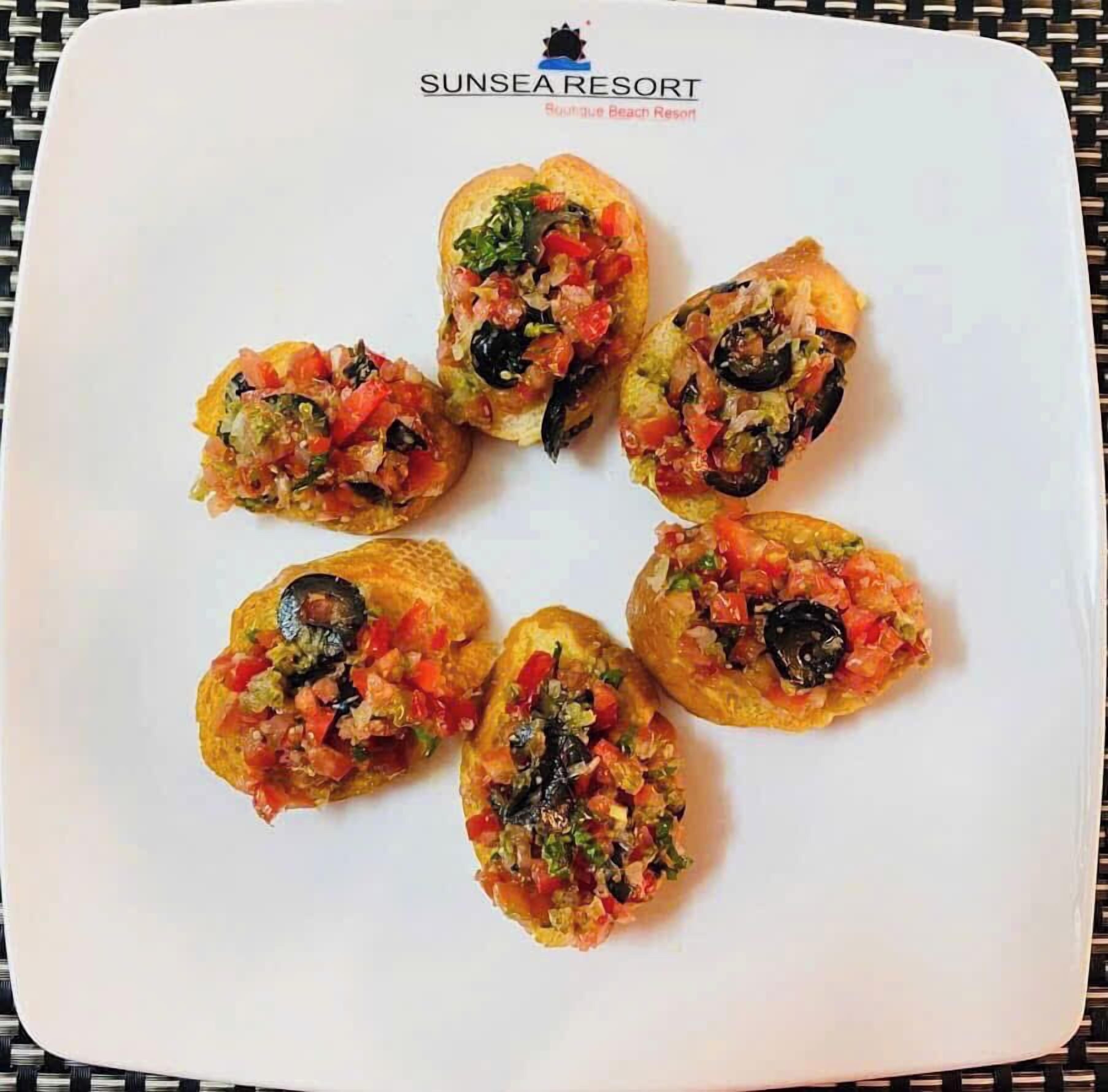 A white plate with five stuffed mushrooms garnished with a colorful topping, placed on a table with a woven tablecloth.