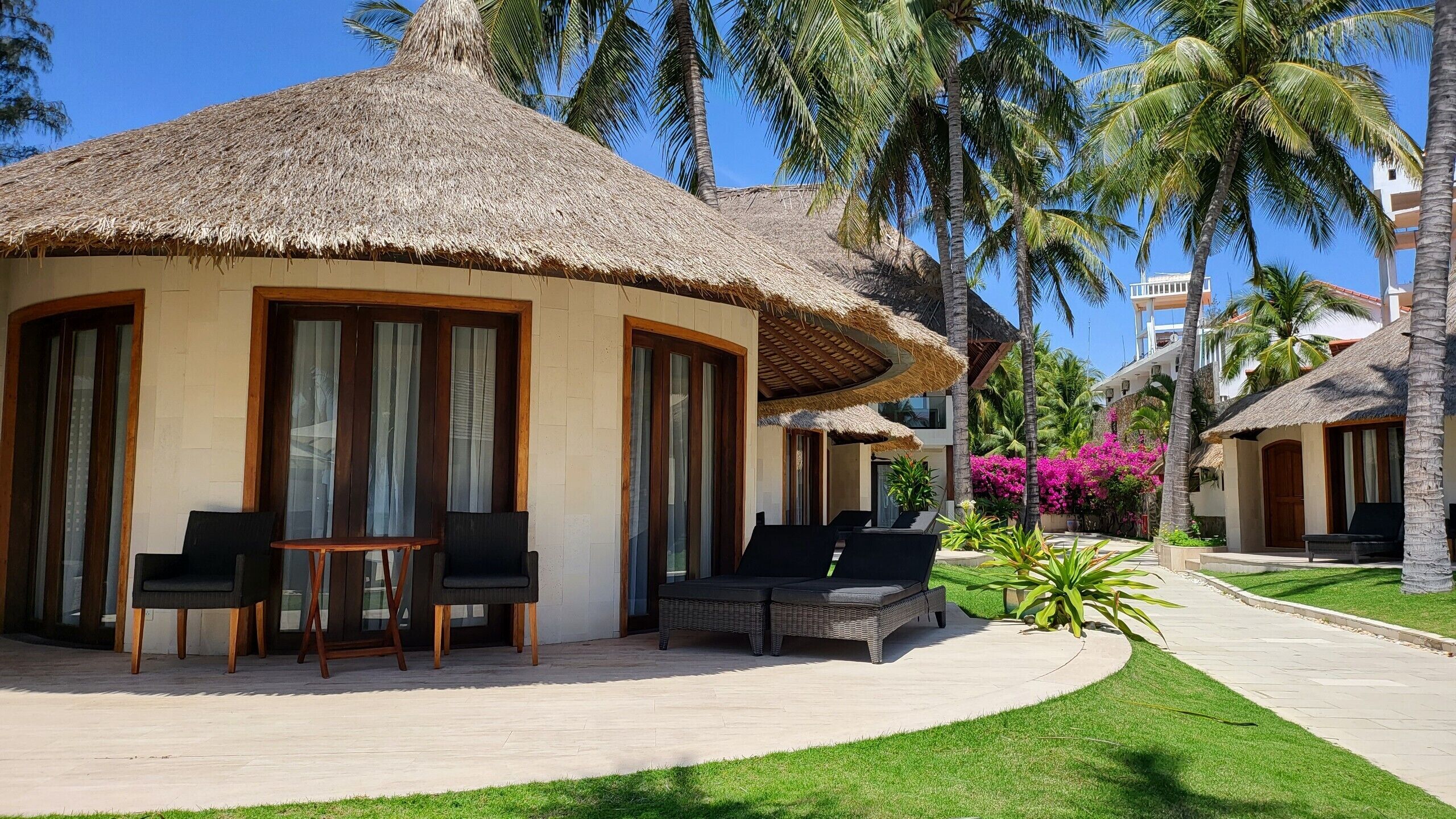 Un resort con villas de techo de paja, mobiliario exterior y exuberante vegetación.