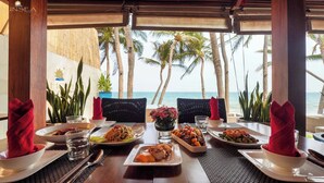 A dining table with various dishes, a view of the ocean, and palm trees. - Sunsea Resort (Mui Ne)