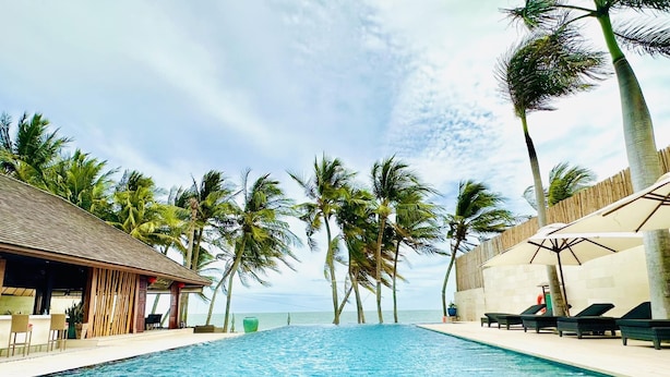 A pool area with lounge chairs and a building with a sloped roof. - Sunsea Resort (Mui Ne)