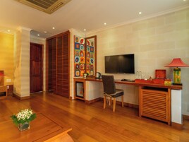 A modern living room with a wooden floor, a TV mounted on the wall, a desk with a chair, and a decorative wall piece.